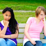 Two bored teenage girls sitting on bench